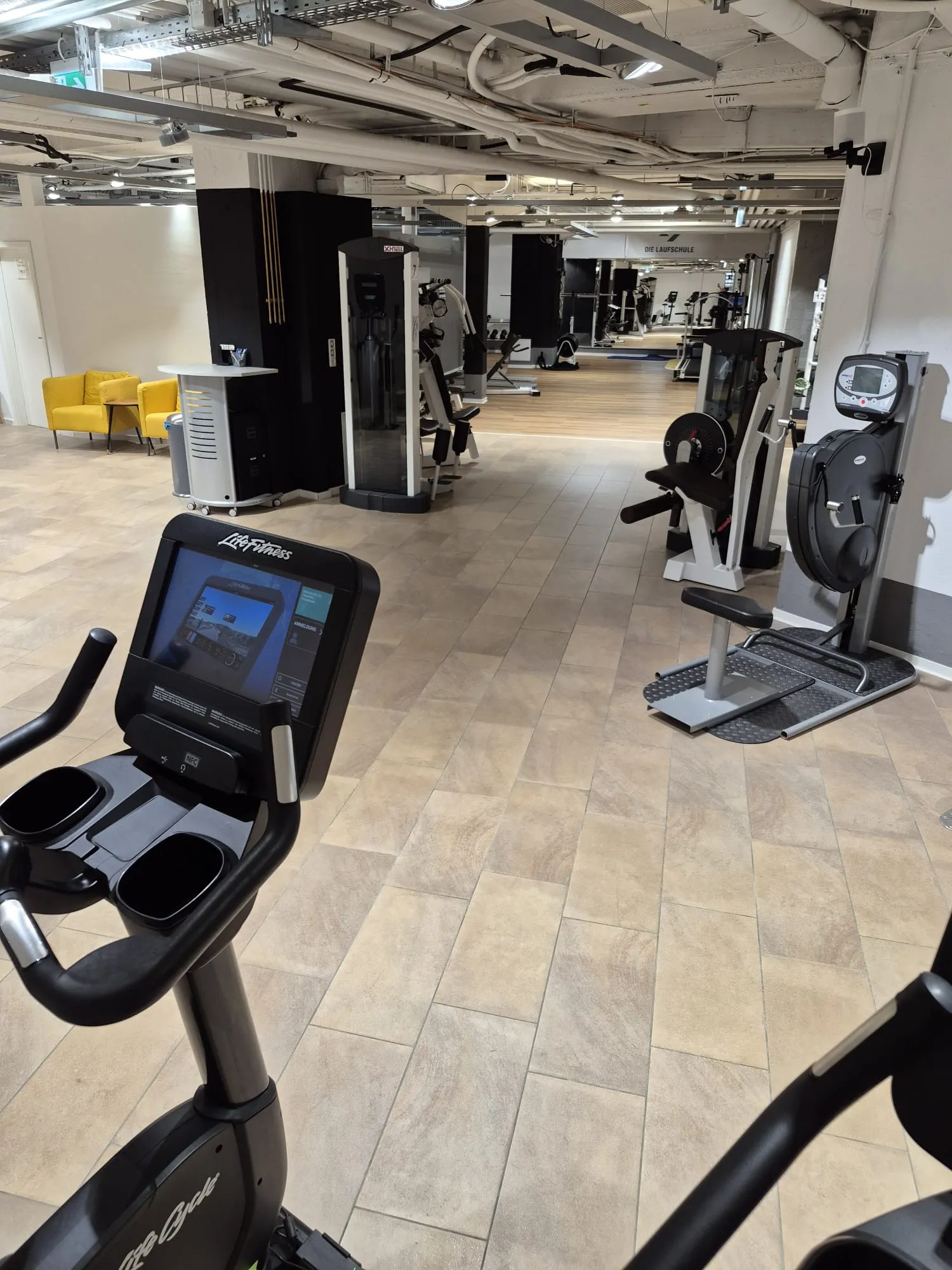 Fahrradergometer im Cardiobereich am Holzweg in Oberursel, dahinter gelbe Sessel
